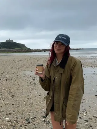 Dua Lipa trägt am Strand eine Wachsjacke mit Shorts und einer Baseballkappe