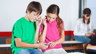 Two kids sharing headphones and listening to music in a cafeteria setting