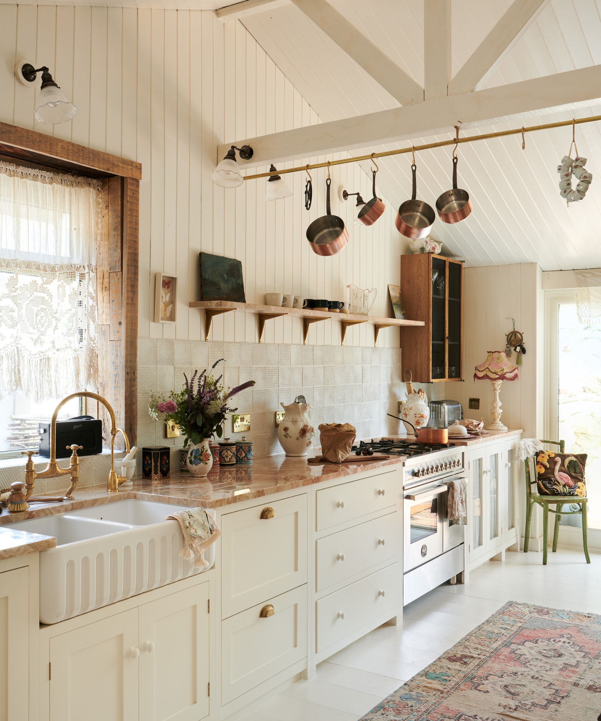 A one-wall country kitchen with white cabinets, white shiplap paneling on the walls, and copper pots hanging from the ceiling beams