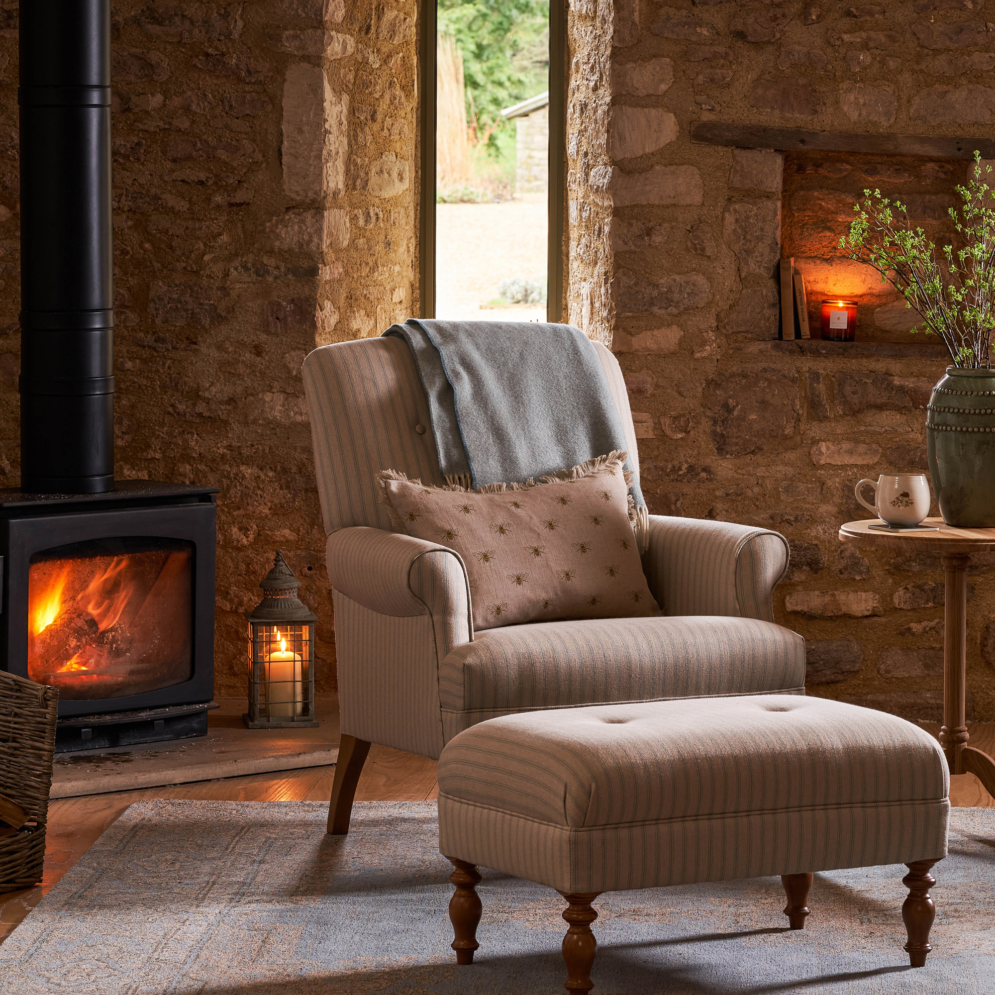 cosy living room with striped wing-back armchair and log burning stove with exposed stone walls
