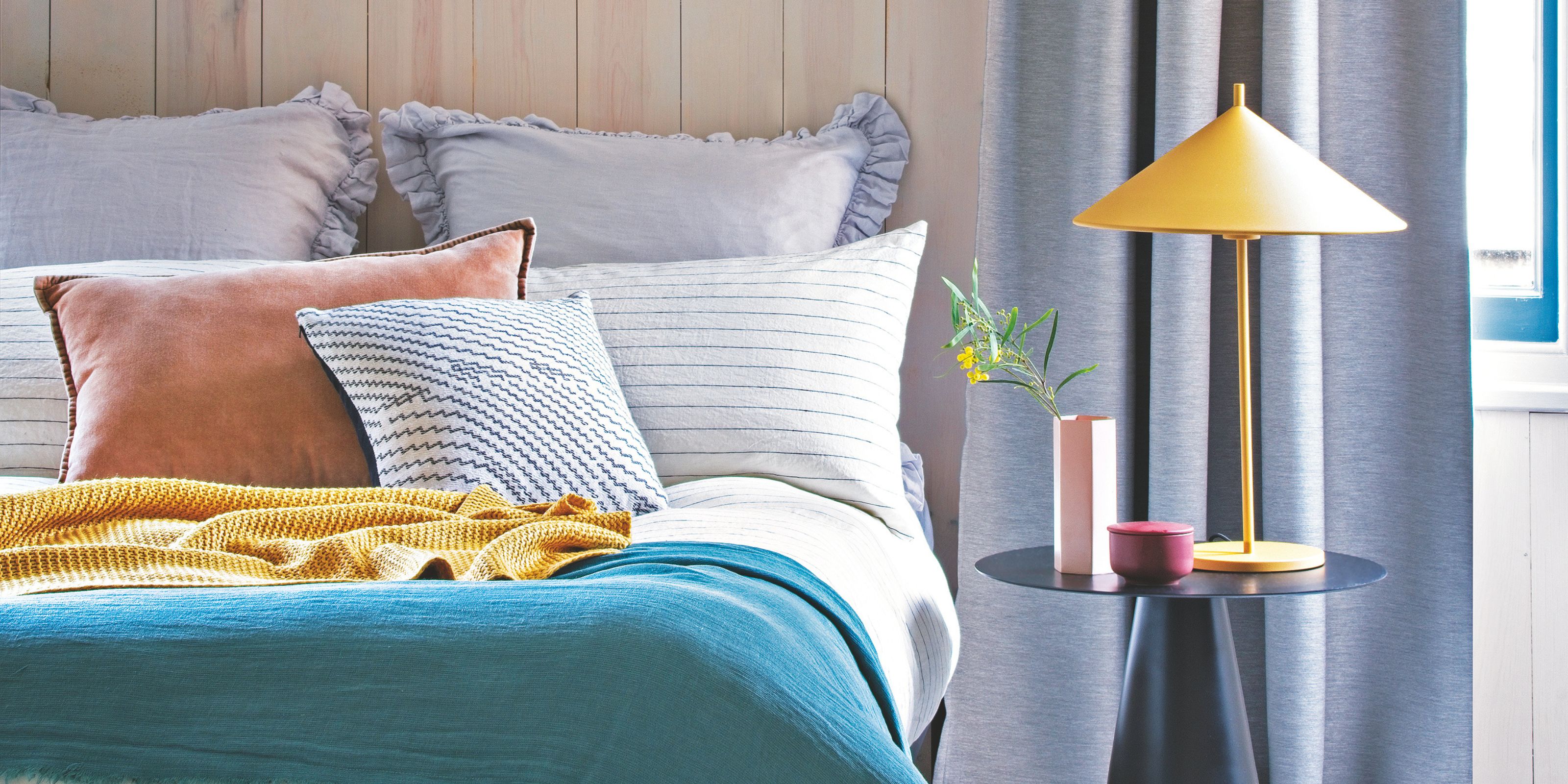 A bed and bedside table with a yellow lamp and pink vase on it
