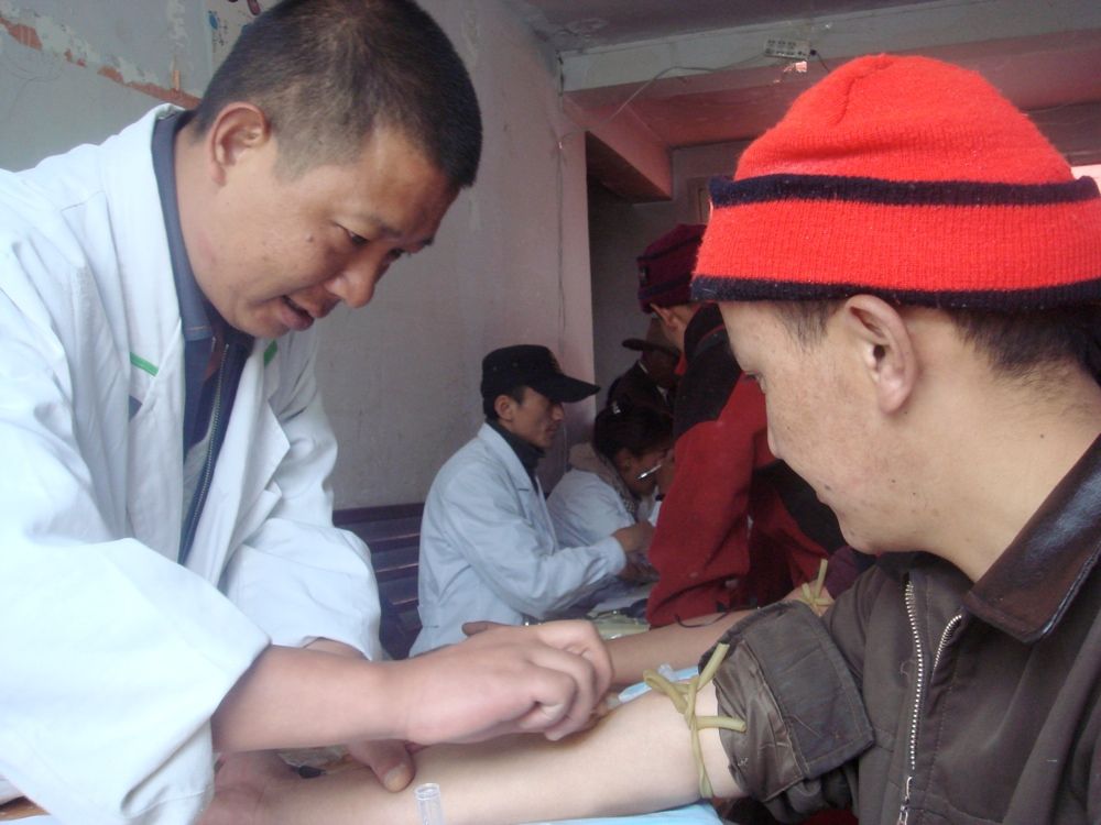 A researcher collects a blood sample from an ethnic Tibetan man participating in a DNA study.