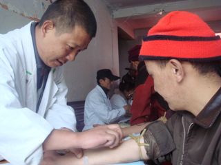 A researcher collects a blood sample from an ethnic Tibetan man participating in a DNA study.