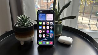 Apple iPhone 16 Pro smartphone next to Airpods case with apps on screen