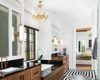 Master ensuite bath with gold and crystal chandelier wooden vanities and geometric black and white flooring