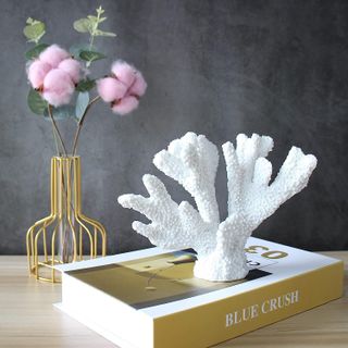 white coral reef decor piece sitting on a coffee table book with a vase of flowers nearby