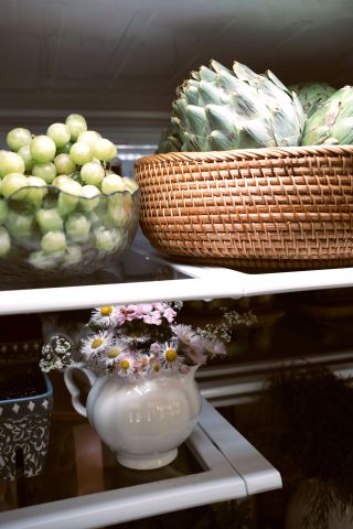 glass bowl with grapes and rattan bowl with artichokes sitting on shelves in an open fridge.