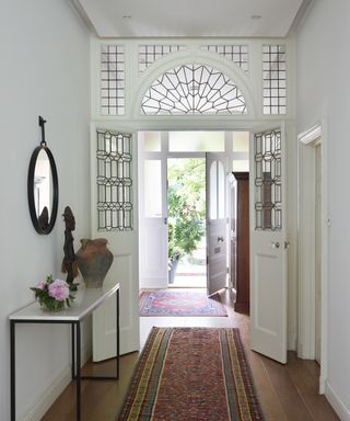 A hallway carpet idea with Persian-style rugs on a wooden floor with white walls and glass arch over walkway