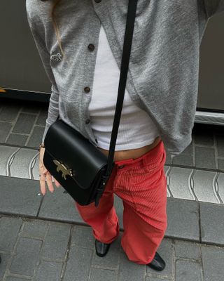 Woman wearing a gray cardigan with a white tee and red corduroy pants.