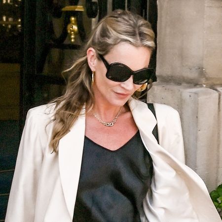 Kate Moss wearing a cream blazer, black slip dress, and ballet flats while exiting a hotel in Paris