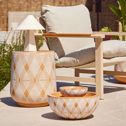 Terracotta water feature on a white patio with beige outdoor dining set