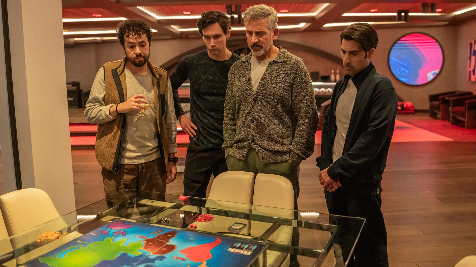 L-R: Ramy Youssef, Cory Michael Smith, Steve Carell and Jason Schwartzman standing looking at a RISK board in a scene from HBO Max&#039;s &quot;Mountainhead&quot;