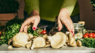 Woman's hands preparing fresh raw oyster mushrooms on kitchen counter with various vegetables