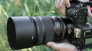 Nikon Z 135mm Plena lens in photographer's hands outside with grassy background