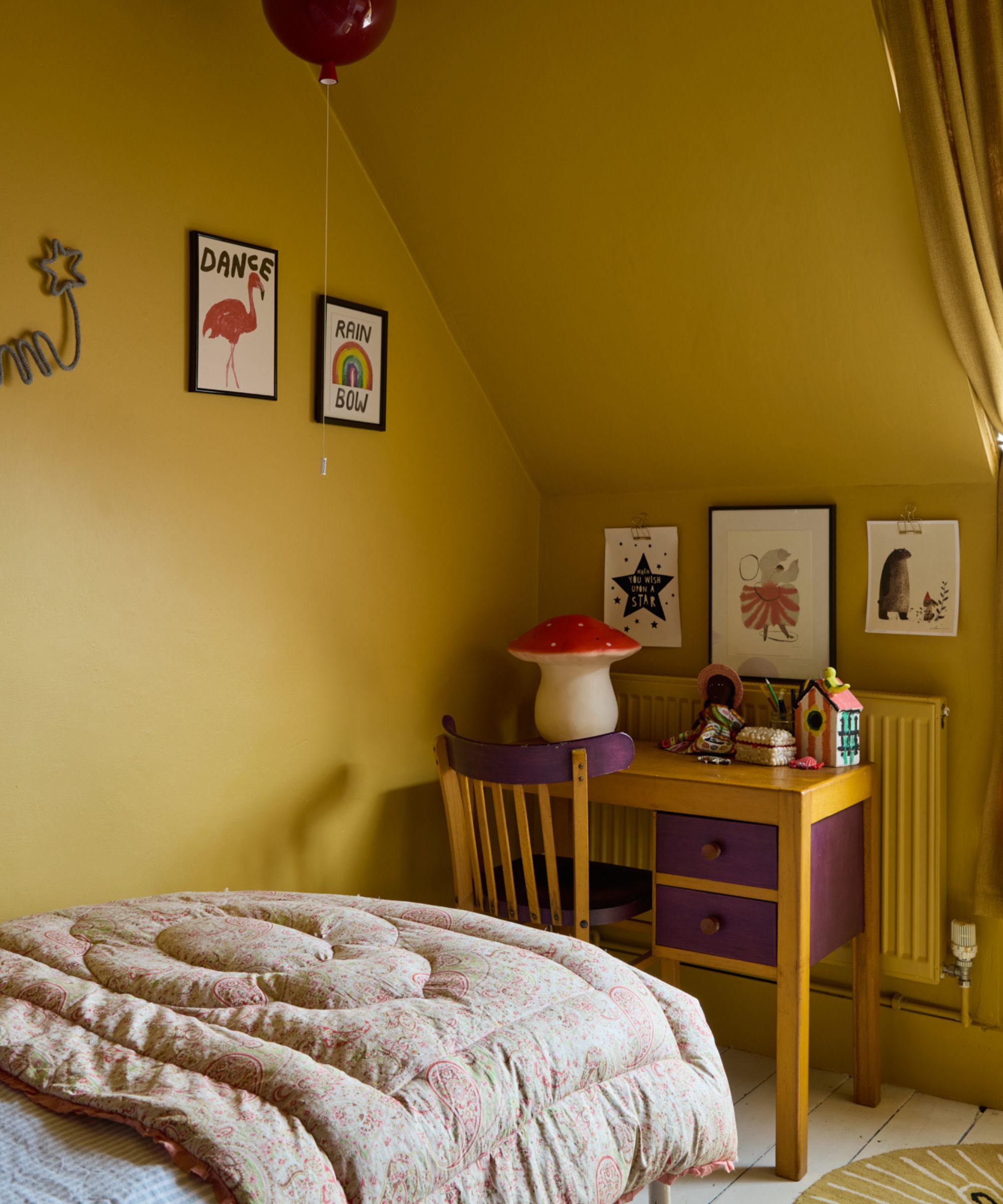 Mustard yellow bedroom wall paint with desk, sloping room, single bed, and artwork on the wall