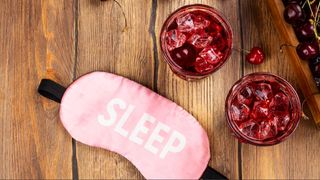 A red drink surrounded by cherries and a pink sleep mask.