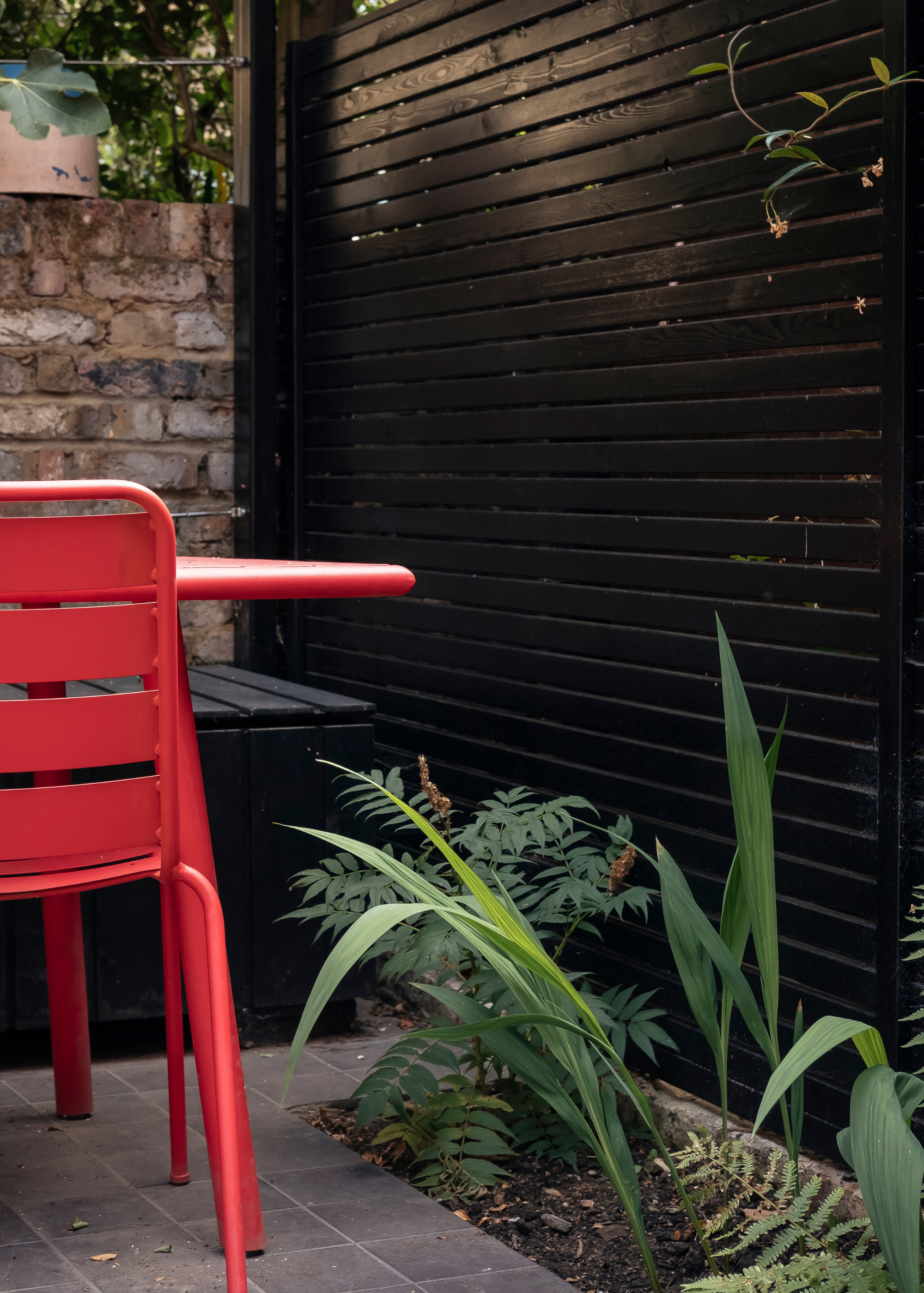 a small urban garden with a black painted fence and bright red furniture