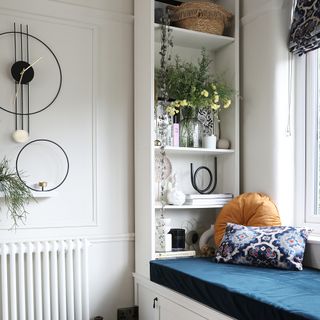 White shelving with plants, flowers and books at end of window seat