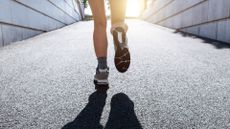 Reverse of woman's legs Jeffing, running towards sunlight on gravel path
