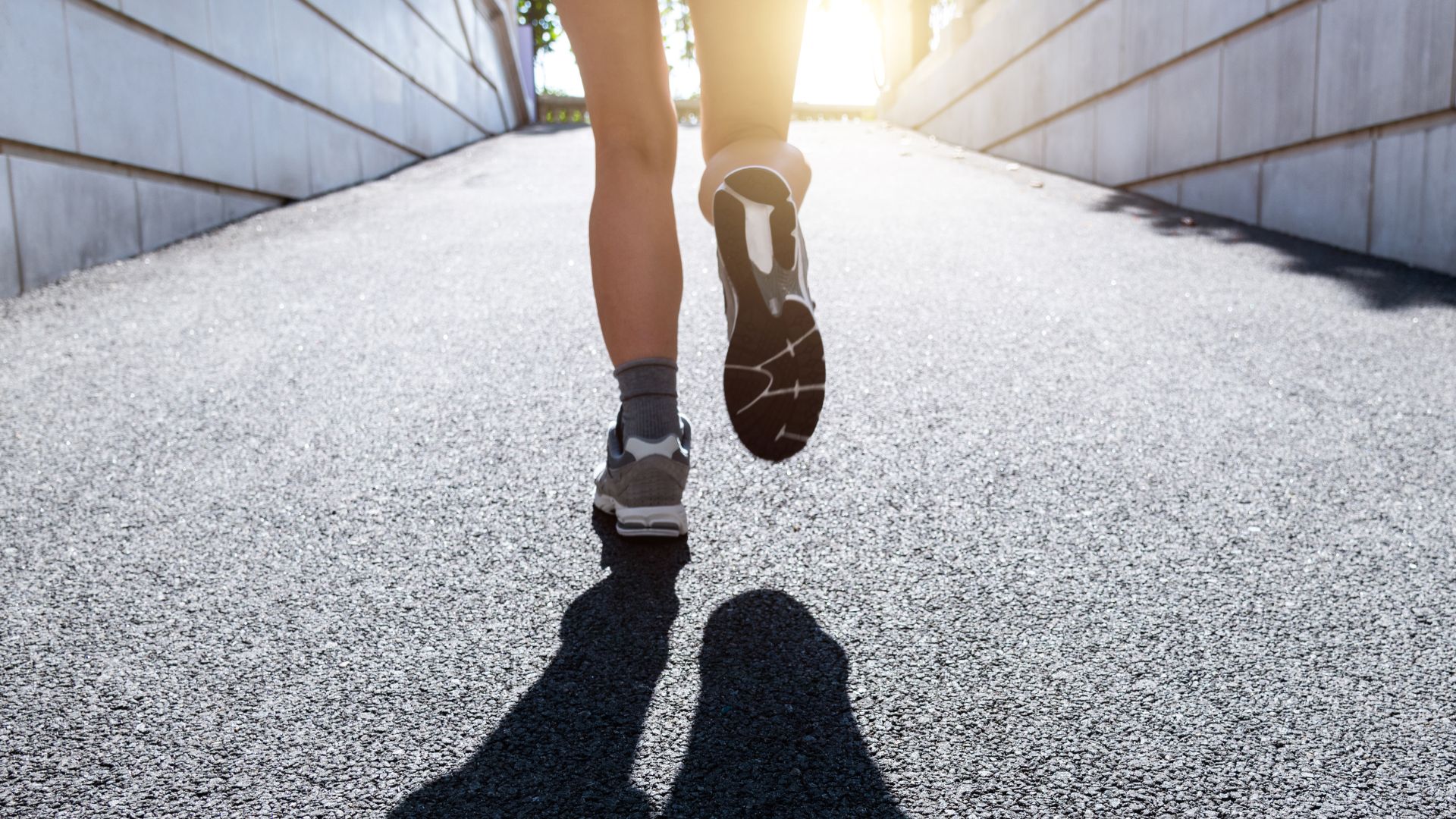 Reverse of woman's legs Jeffing, running towards sunlight on gravel path