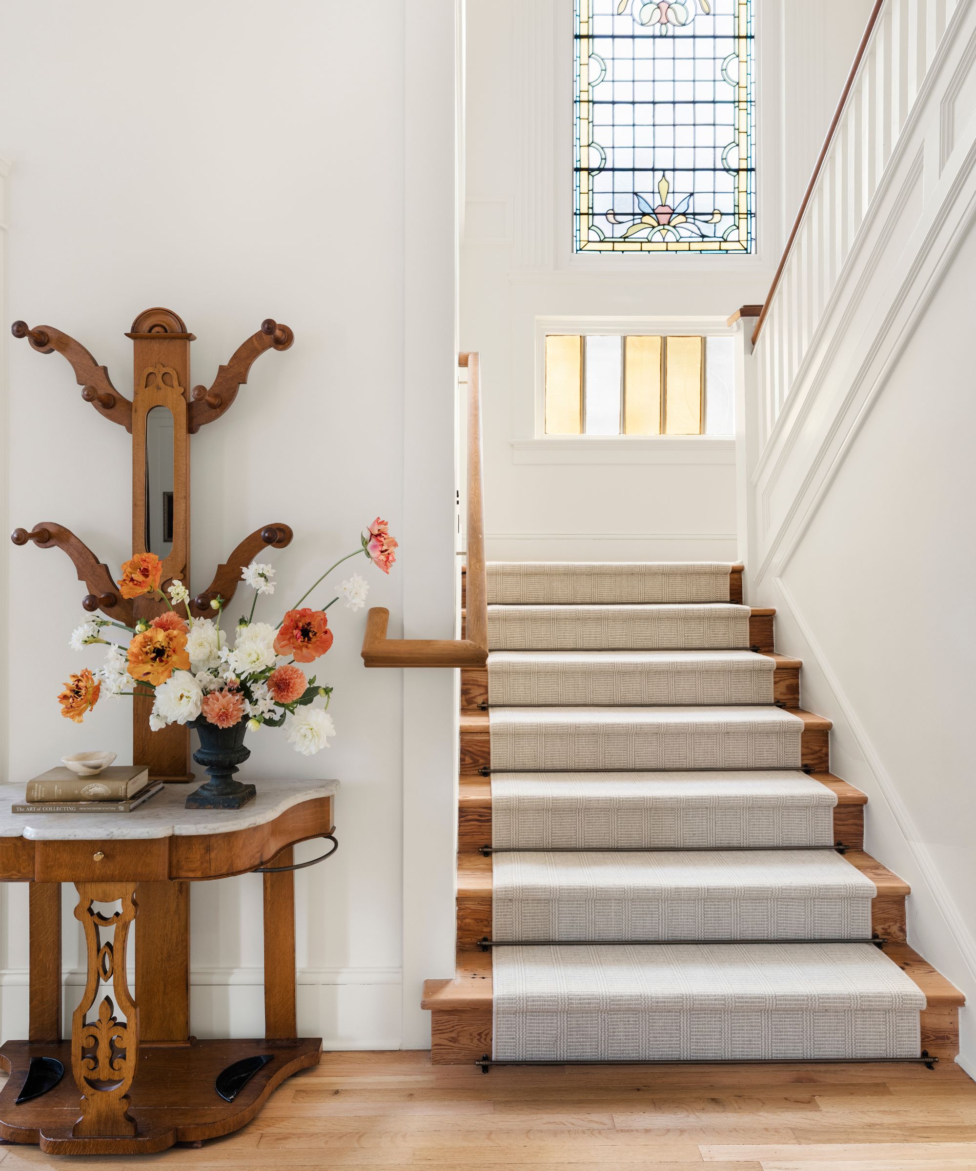 a light and bright hallway with a grand staircase with original stained glass window at the top