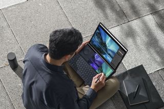 Man seen from above sat on pavement working on ASUS ZenBook Pro Duo