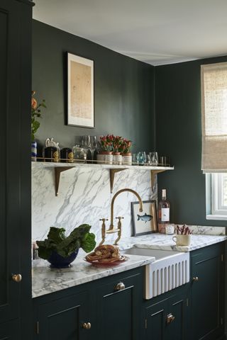 A small kitchen with a marble splashback and deep green cabinets