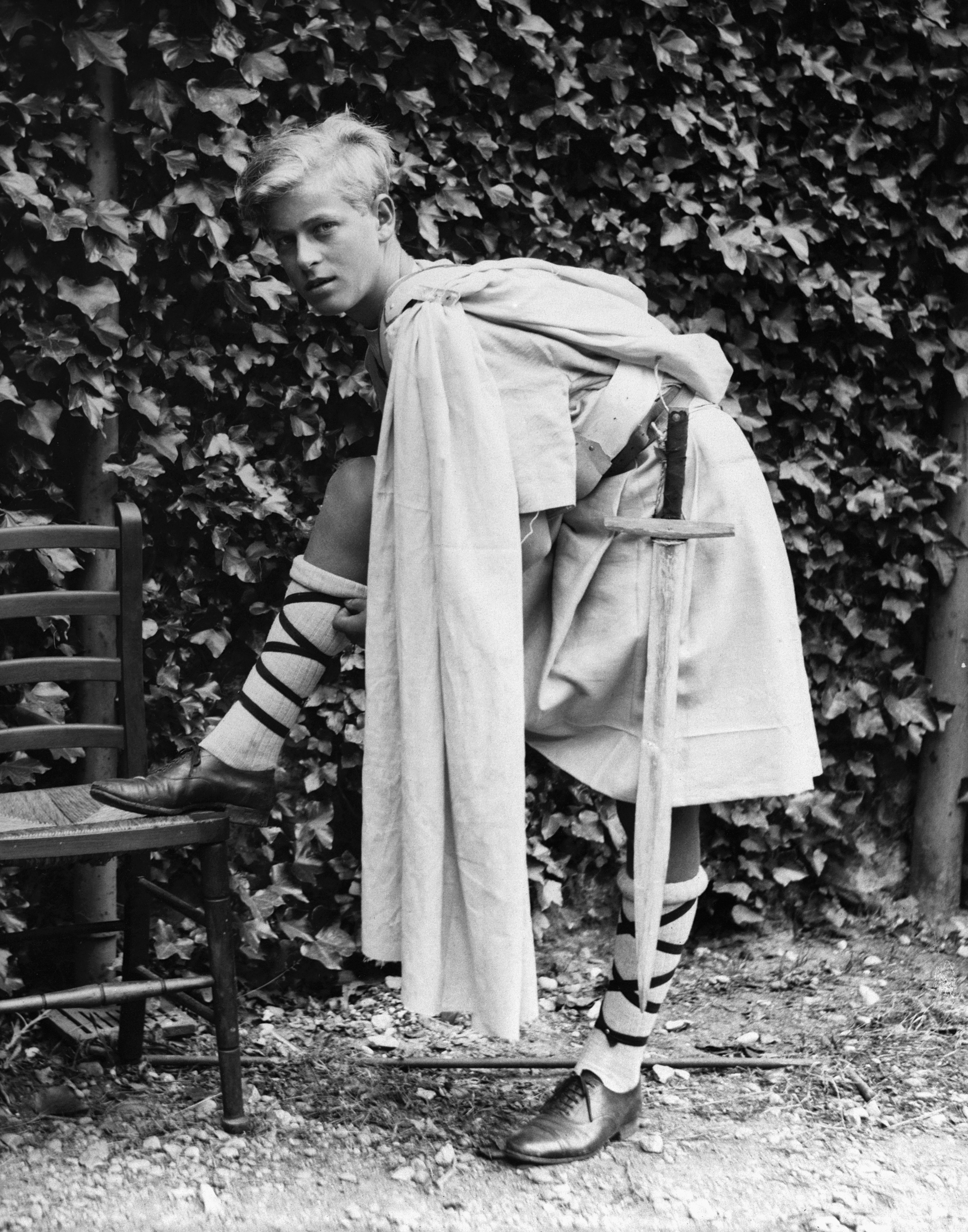 Prince Philip in a toga putting his foot on a chair as a teenager