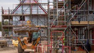 A house being constructed with a yellow JCB in the foreground