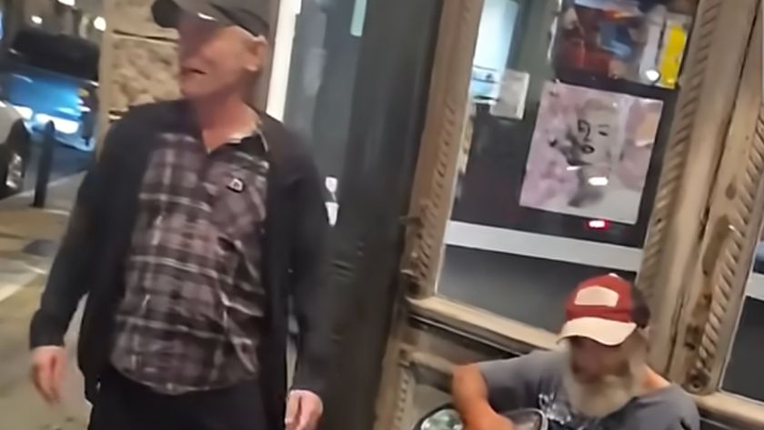 Bruce Dickinson on a street corner, next to a bearded man with an acoustic guitar