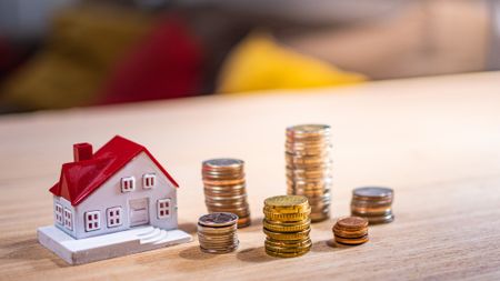 Small model home sitting on a table next to several stacks of coins