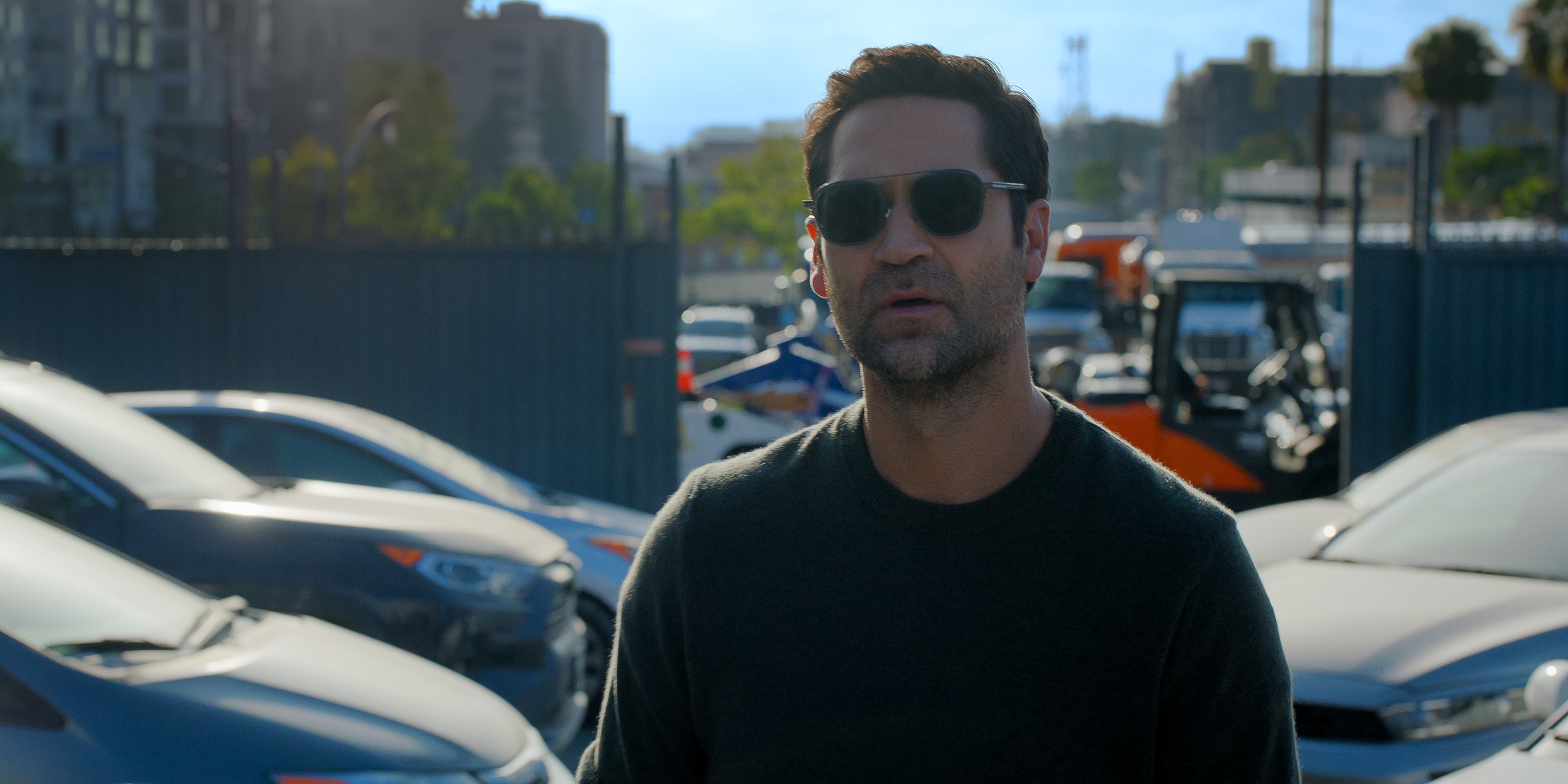 Manuel Garcia-Rulfo as Mickey Haller in episode 410 of The Lincoln Lawyer wearing sunglasses and walking through a car lot