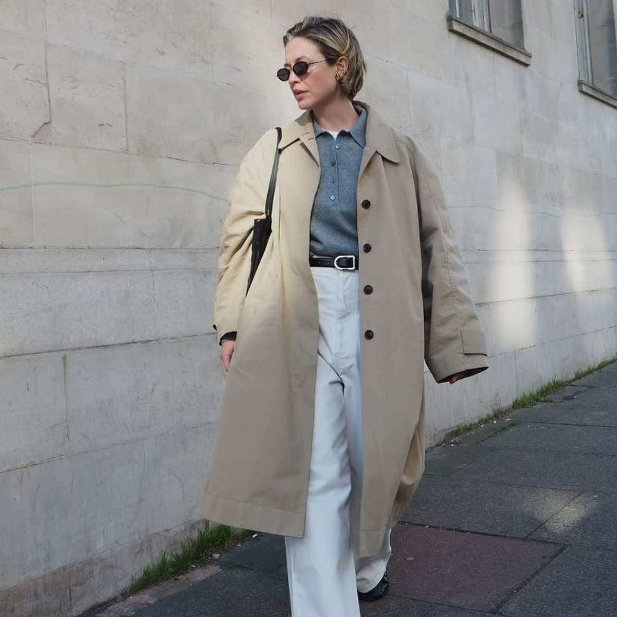 Alexis in a trench coat, grey collared top and white jeans