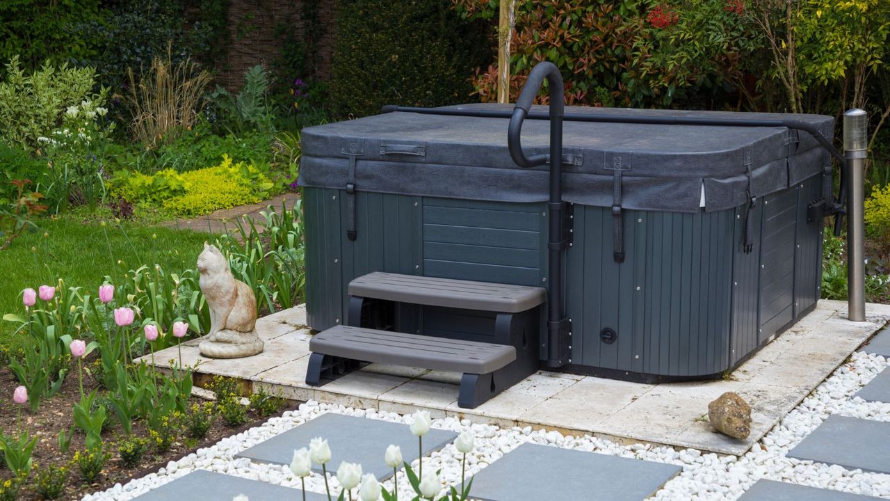 A black hot tub in a yard with tulips and statues