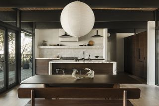 An open plan kitchen diner with a marble island, a large lamp shade, and a dark wooden dining bench