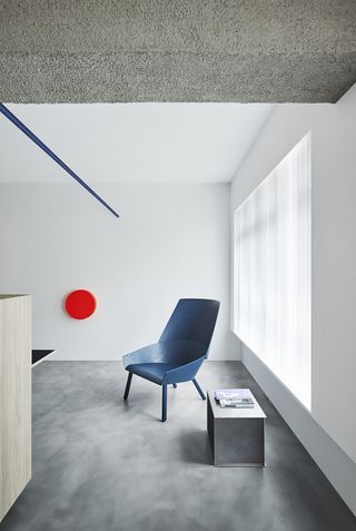 Interior of Alex's apartment in Singapore with white walls, grey floors and blue chair