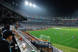 A wide shot of fans watching New York City FC playing New York Red Bulls on a rainy night at Citi Field, Queens