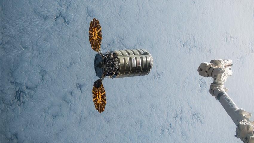 a spacecraft with two solar wings above earth. at right is a robot arm