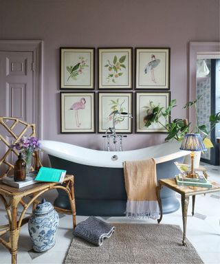 A pink bathroom idea with navy freestanding bath, framed bird wall art, a rattan chair, lampshade