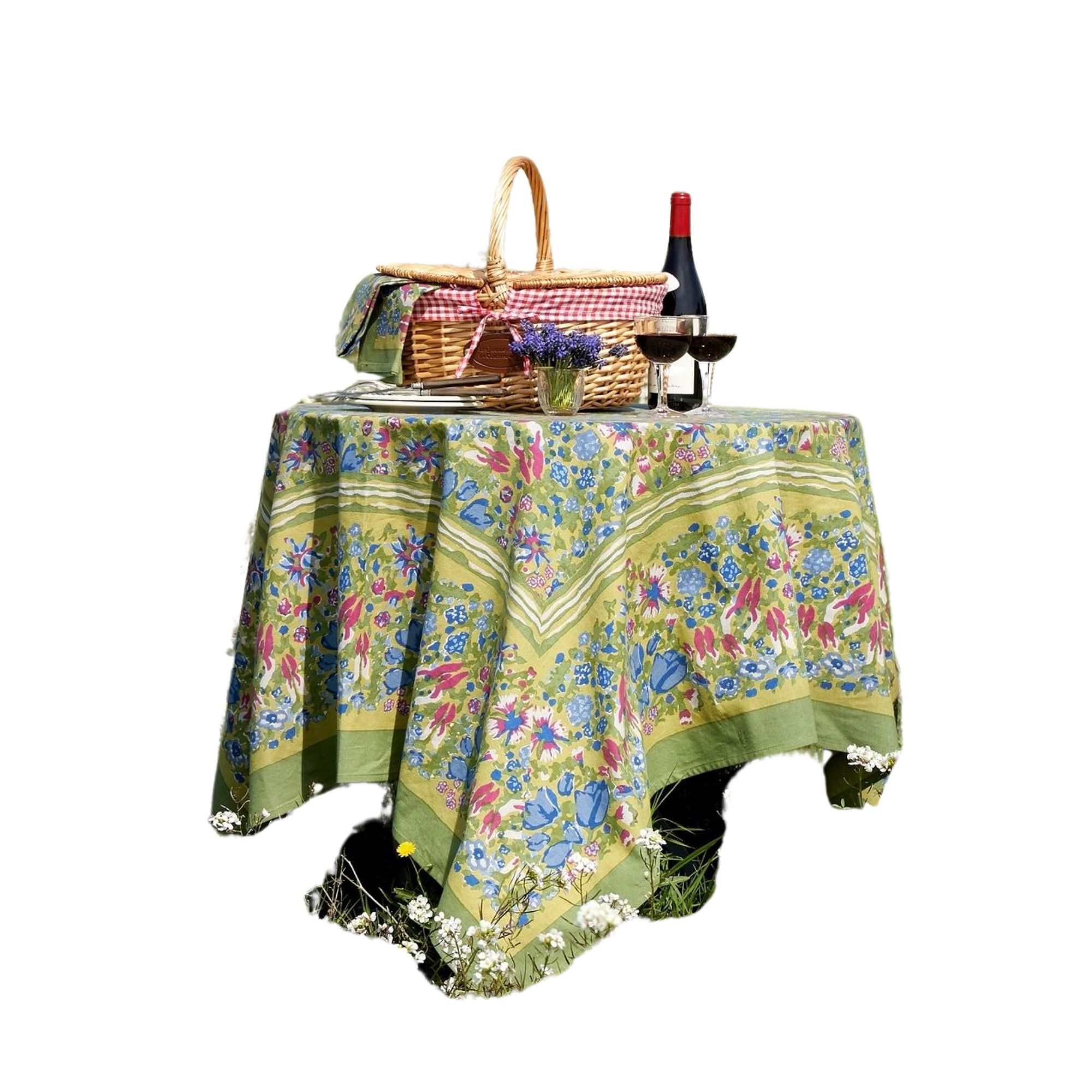 A green tablecloth with a blue and red floral pattern on it, and a basket and wine glasses on top of it
