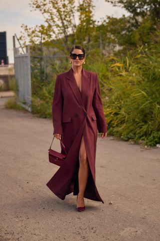 A woman wearing a burgundy long blazer coat, burgundy slingback heels, large sunglasses, and a burgundy bag.