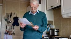 An older man opens and reads his mail in the kitchen.