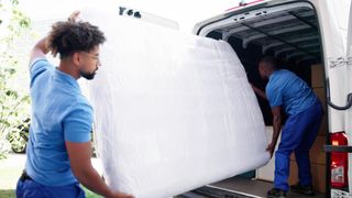 Two people place a covered mattress in a van to move it to a new house