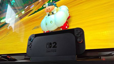 Nintendo Switch 2 sitting on black TV bench with Mario Kart World gameplay in backdrop featuring Cow.