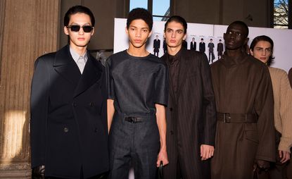 Five male models wearing clothing by Salvatore Ferragamo in dark shades.