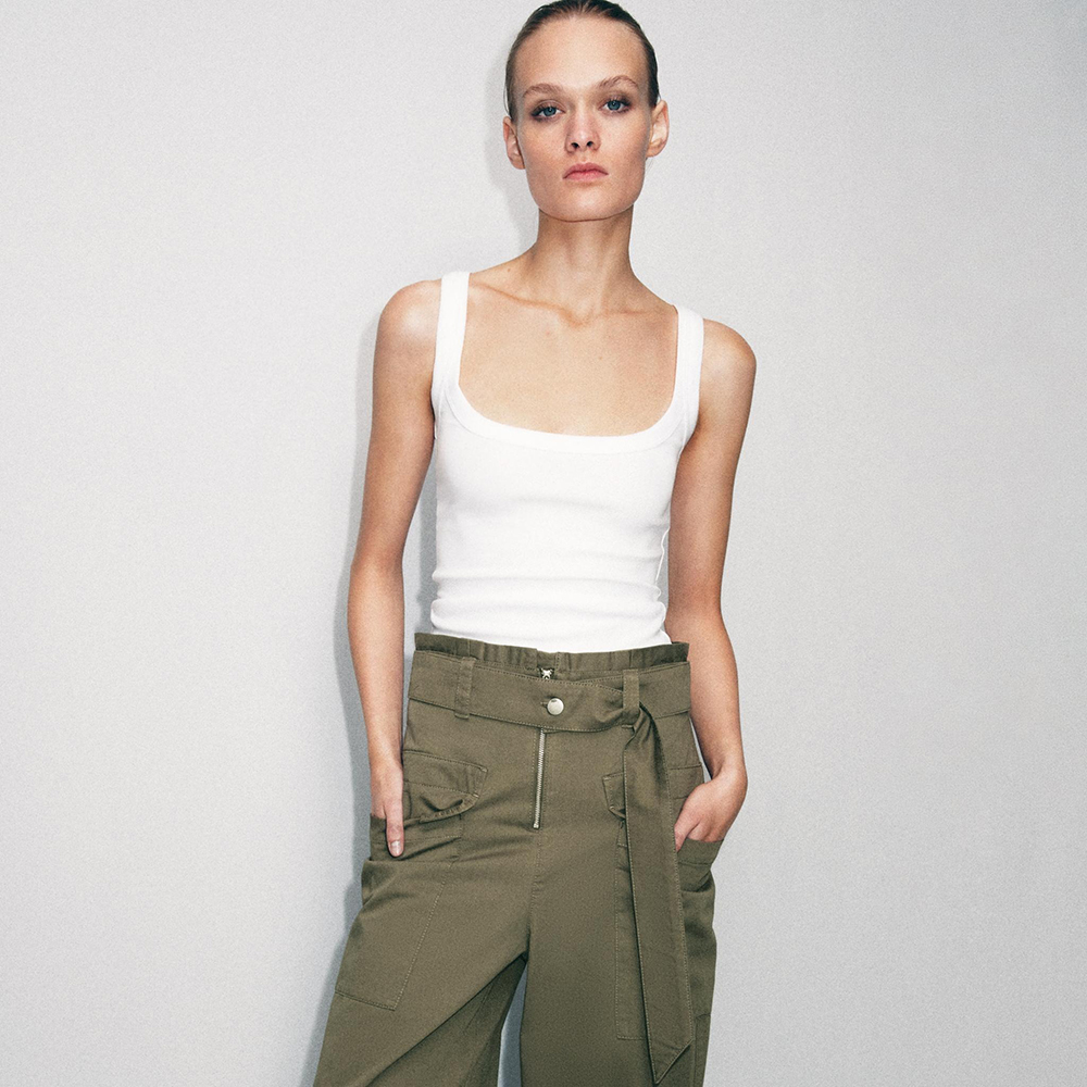 a model wearing a white tank and green pants