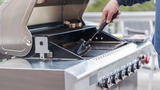 Man cleaning a gas grill with brush
