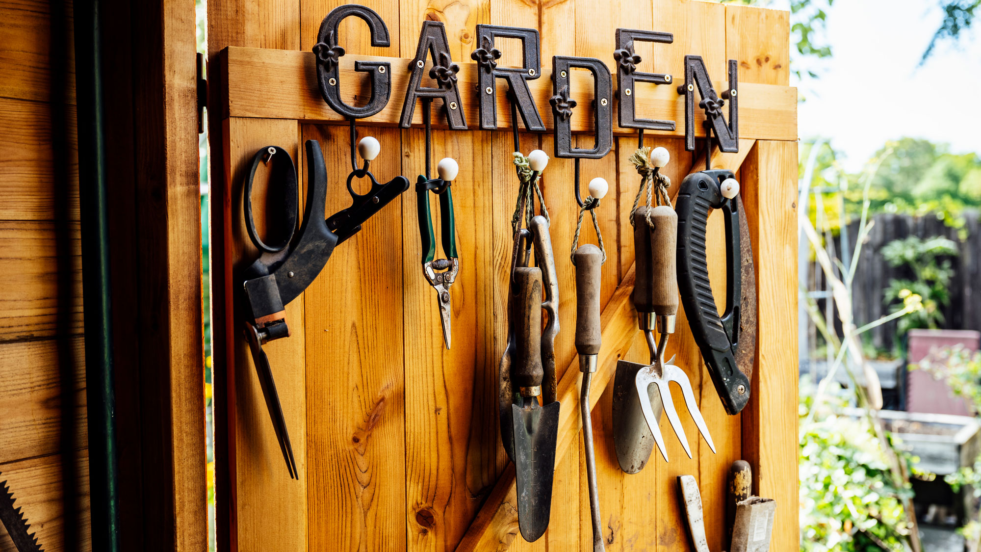 assorted garden tools hanging from rustic wooden shed door with garden sign