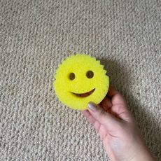 Holding a yellow Scrub Daddy sponge in front of cream carpet