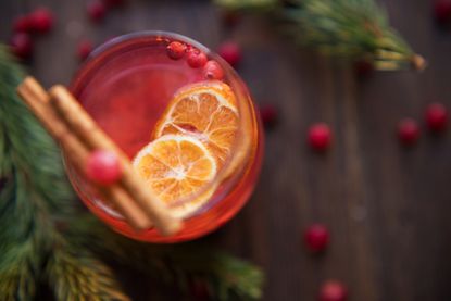 Mulled wine with cinnamon and cranberry on vintage wooden table with red berries and green spruce branches